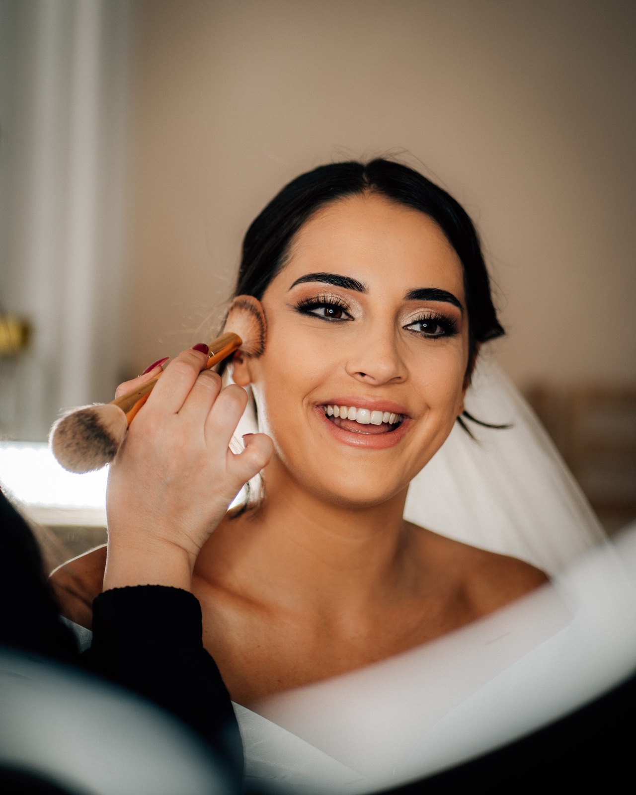 Lachende Braut beim Make-up, Schleier bereits gesteckt